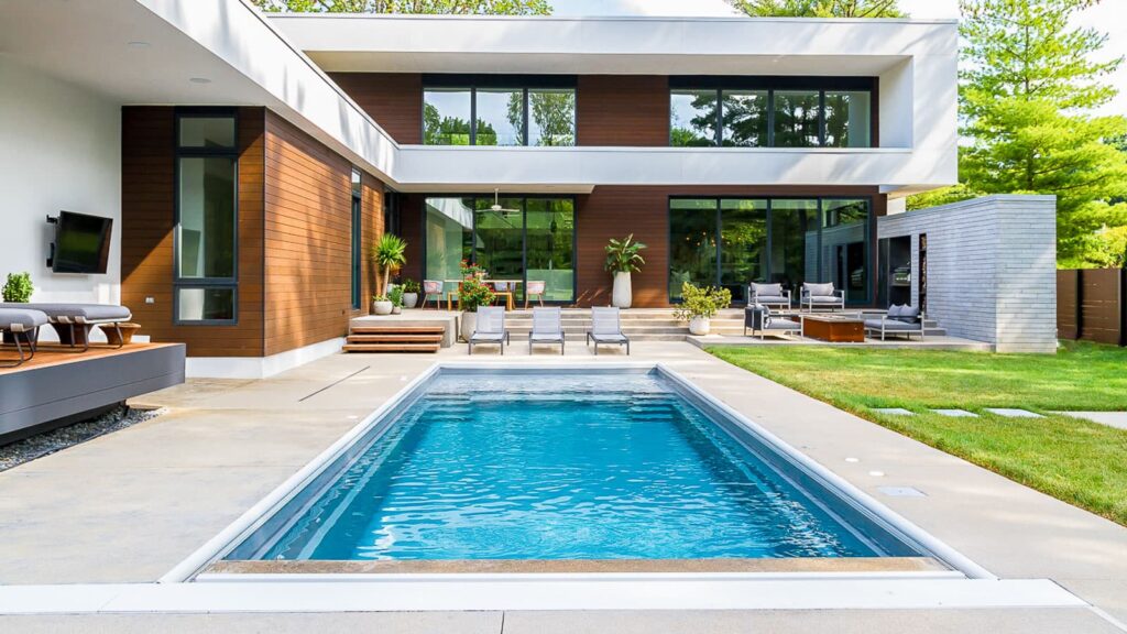 A modern home featuring large windows and a sleek design, with a swimming pool in the foreground. The backyard includes lounge chairs and greenery, creating a spacious outdoor area.